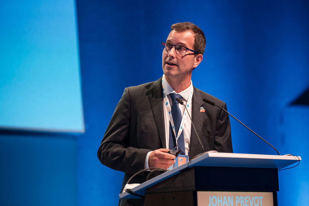 IPIC2023: A man in a suit and tie stands at a podium, addressing an audience with a focused expression.