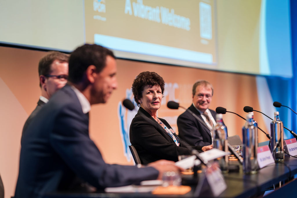 IPIC2023: A panel of individuals seated at a table, each with a microphone, engaged in discussion.