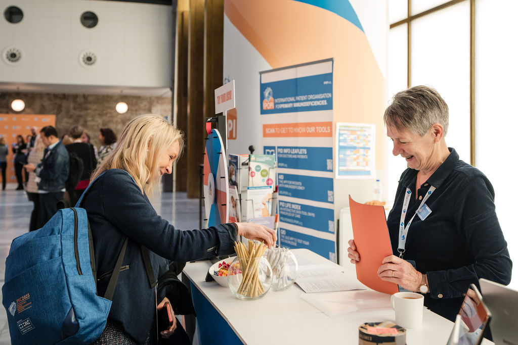 IPIC2023: At an admission desk, two women talk and look at information from a blue folder.