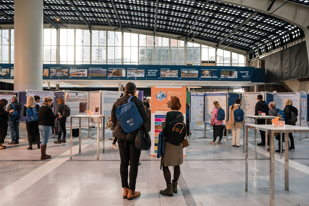 IPIC2023: Attendees browse various research posters displayed at a conference poster session inside a large, well-lit exhibition hall.