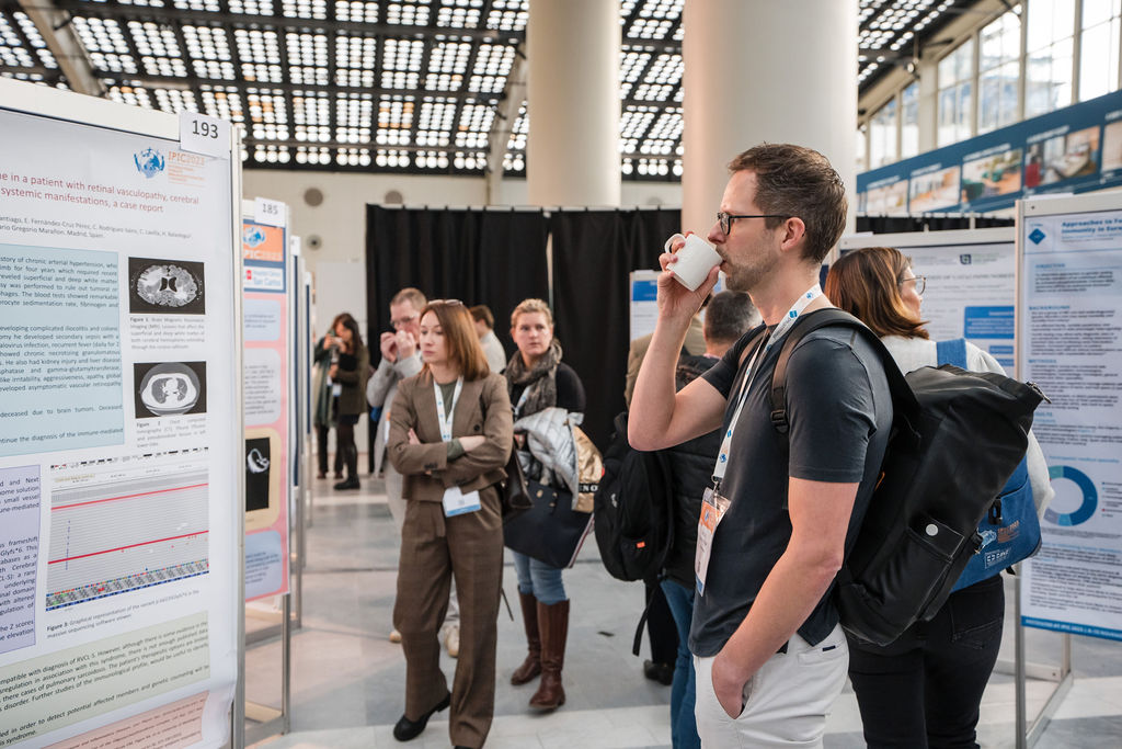 IPIC2023: A man sips a drink while looking at a scientific poster, surrounded by other attendees