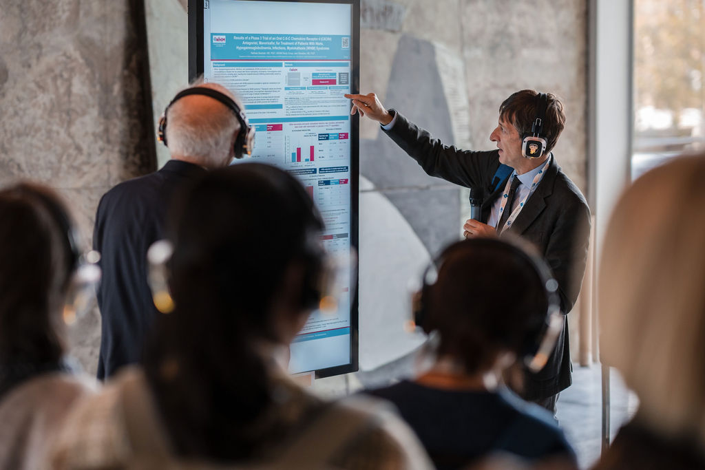 IPIC2023: A presenter points at a digital poster while an audience listens through headphones.