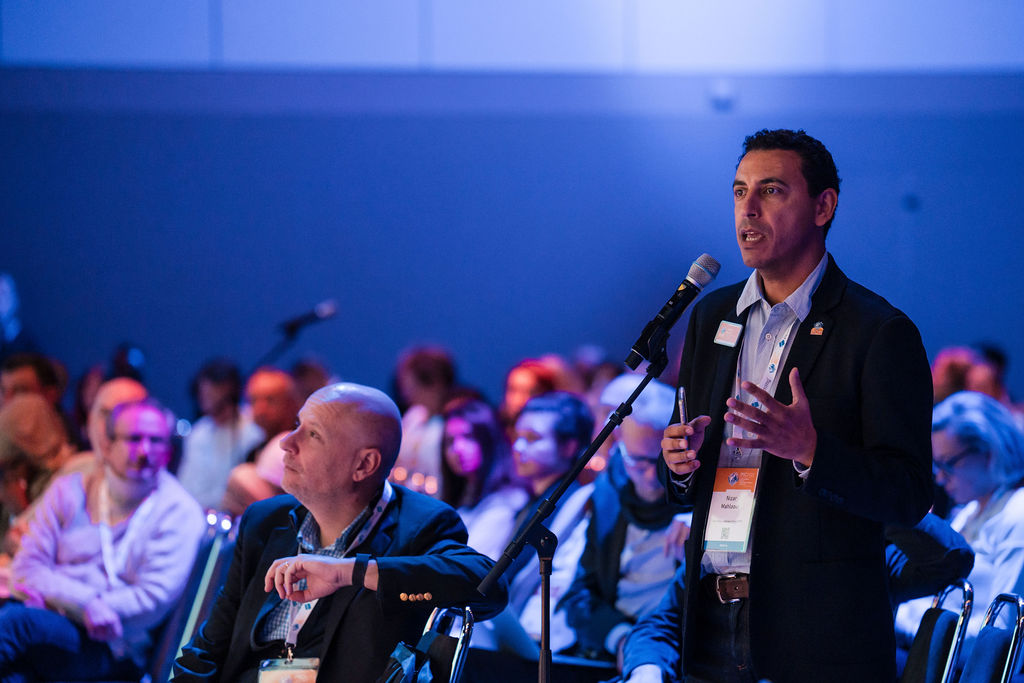 IPIC2023: A man delivers a speech at a conference, engaging a captivated audience in the background.