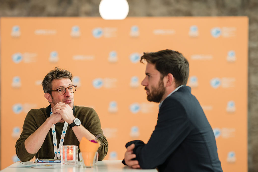 IPIC2023: Two men having a conversation at a table at IPIC2023