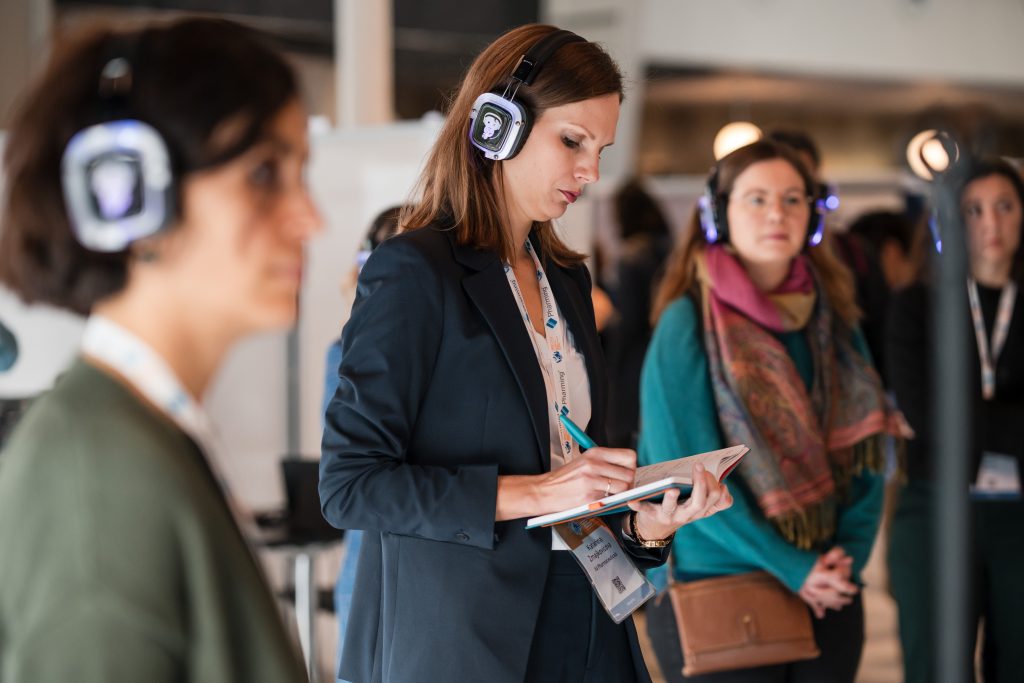 Sponsorship Proposal: A woman wearing headphones takes notes, focused on a notepad in her hands_Sponsorship_ Proposal