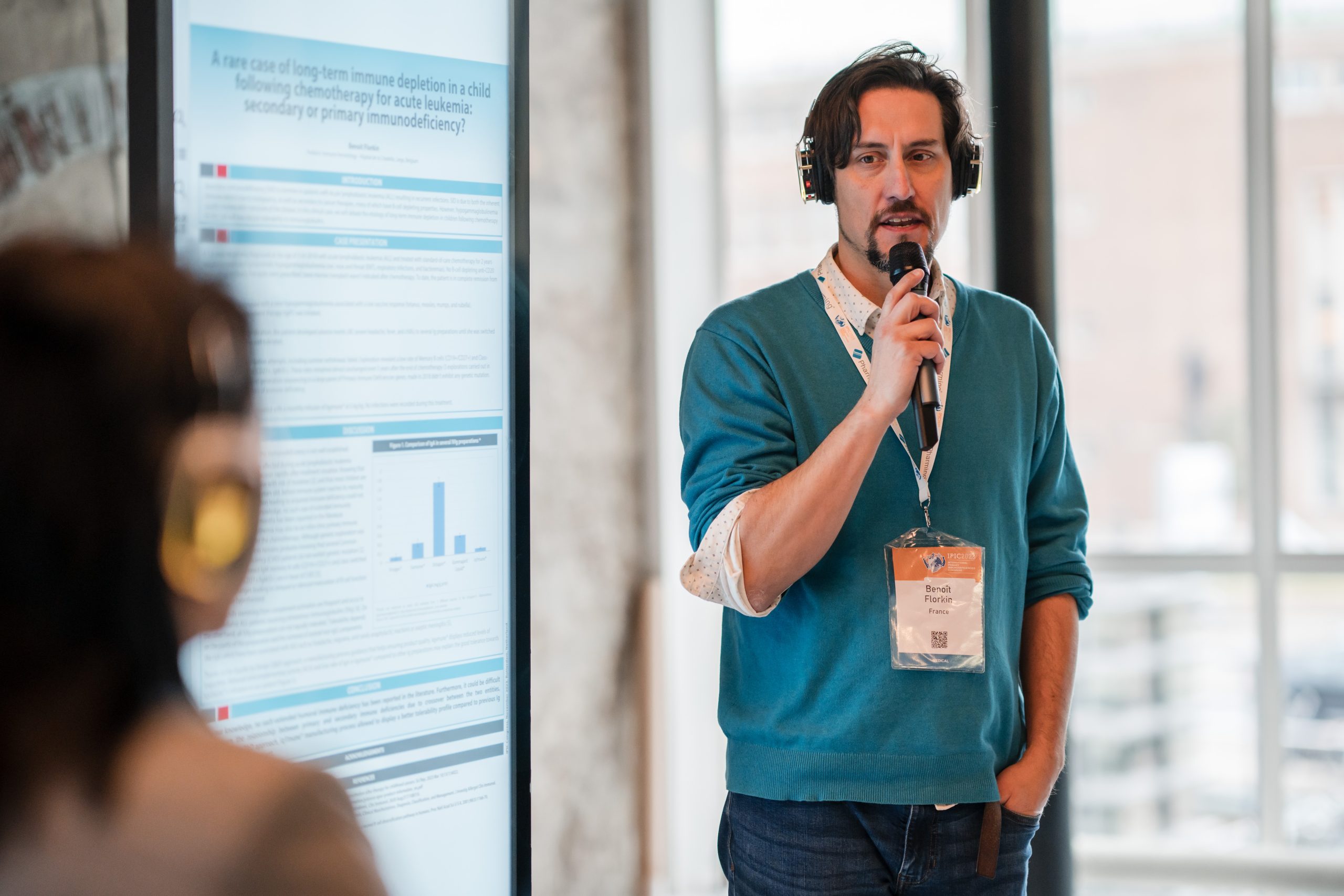 Sponsorship Proposal: A man addresses an audience while speaking into a microphone, with a poster displayed behind him